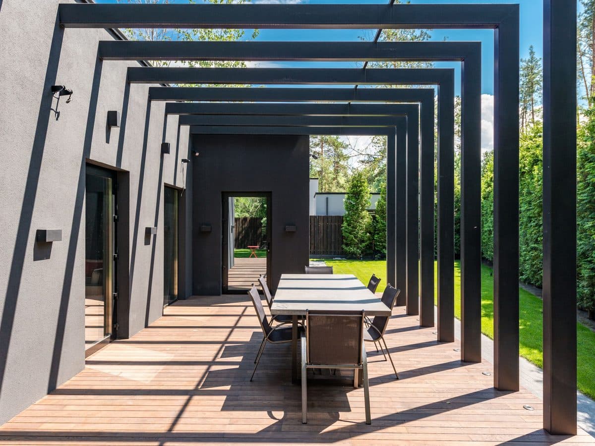Long pergola over an outdoor dining terrace beside a modern home